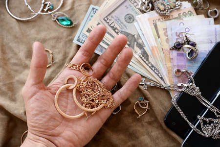 Marauders hand with a bunch of stolen jewelry, money and smartphones on military uniform cloth...