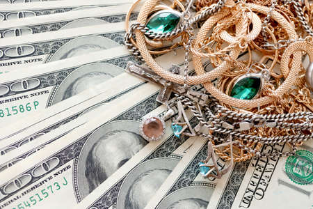 Many expensive golden and silver jewerly rings, earrings and necklaces on big amount of US dollar bills close up. Pawnshop or jewelery shop conceptの写真素材