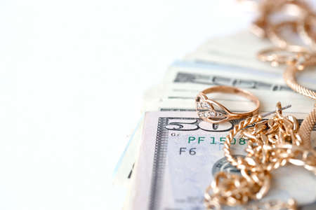 Many expensive golden jewerly rings, earrings and necklaces with big amount of US dollar bills on white background. Pawnshop or jewelery shop conceptの写真素材