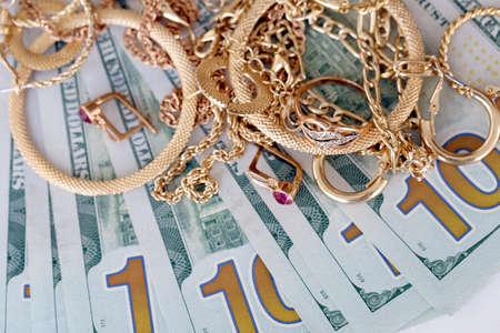 Many expensive golden jewerly rings, earrings and necklaces with big amount of US dollar bills on...