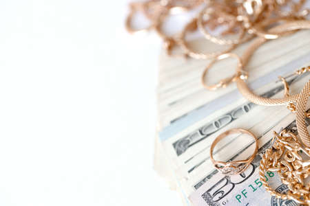 Many expensive golden jewerly rings, earrings and necklaces with big amount of US dollar bills on white background. Pawnshop or jewelery shop conceptの写真素材
