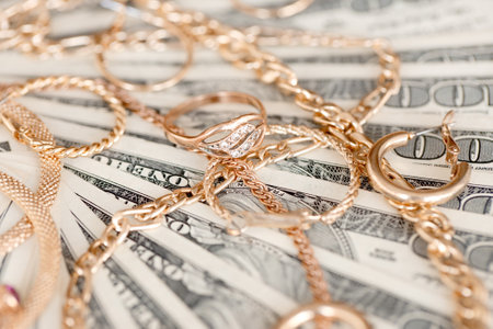 Many expensive golden jewerly rings, earrings and necklaces on big amount of US dollar bills close up. Pawnshop or jewelery shop conceptの写真素材