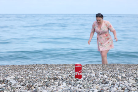 ANTALYA, TURKEY - MAY 18, 2021: Original Coca Cola red tin can lies on small round pebble stones close to sea shore. Coca-cola can and woman on turkish beachのeditorial素材