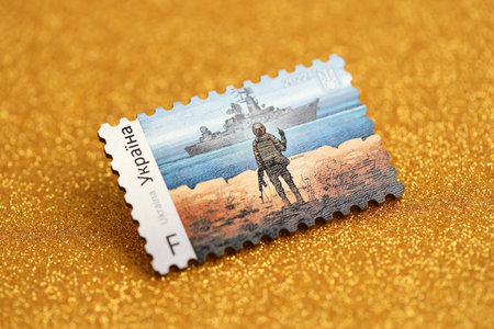 TERNOPIL, UKRAINE - SEPTEMBER 2, 2022 Famous Ukrainian postmark with russian warship and ukrainian soldier as wooden souvenir on golden glitter background surfaceのeditorial素材