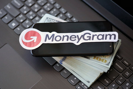 TERNOPIL, UKRAINE - SEPTEMBER 6, 2022 MoneyGram paper logotype lies on black laptop keyboard with US dollar bills. Moneygram is American cross border P2P payments and money transfer companyのeditorial素材