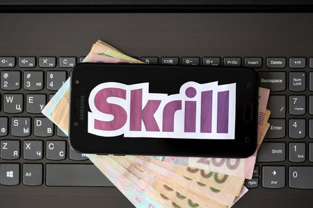 TERNOPIL, UKRAINE - SEPTEMBER 6, 2022 Skrill paper logotype lies on black laptop keyboard with ukrainian hryvnia bills. Payoneer is American financial services company provides online money transferのeditorial素材
