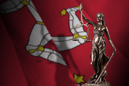 Isle of Man flag with statue of lady justice and judicial scales in dark room. Concept of judgment and punishment, background for jury topicsの写真素材
