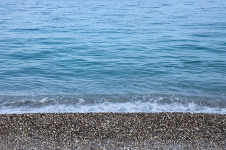 Bank of pebbles with the sea and beach in the background. Pebbles and water on the sea shore in...