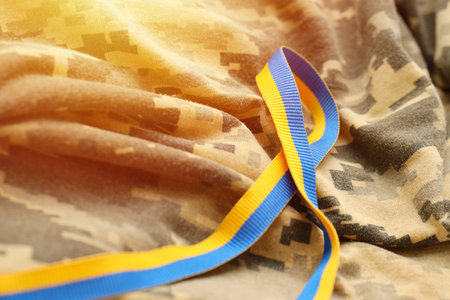 Pixeled digital military camouflage fabric with ribbon in blue and yellow colors. Attributes of ukrainian patriotic soldier uniformの写真素材