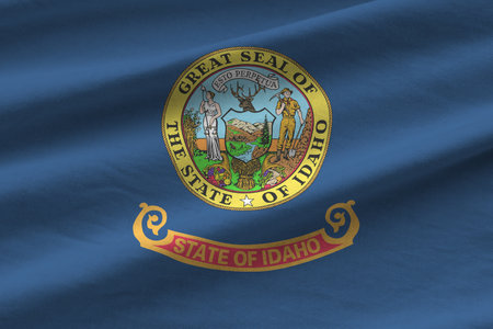 Idaho US state flag with big folds waving close up under the studio light indoors. The official symbols and colors in fabric bannerの写真素材