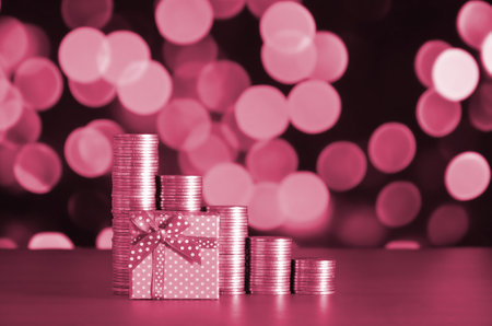 Small red gift box and golden coin stacks on the colored bokeh background. Special offer or cashback...
