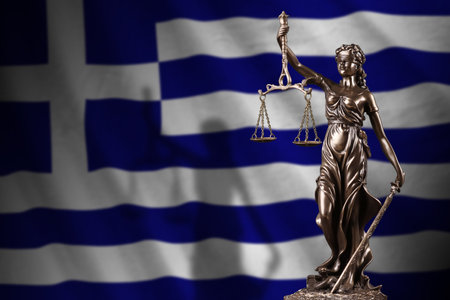 Greece flag with statue of lady justice and judicial scales in dark room. Concept of judgement and punishment, background for jury topicsの写真素材