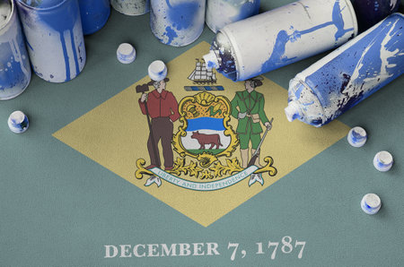 Delaware US state flag and few used aerosol spray cans for graffiti painting. Street art culture concept, vandalism problemsの写真素材