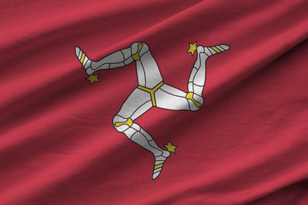Isle of Man flag with big folds waving close up under the studio light indoors. The official symbols and colors in fabric bannerの写真素材
