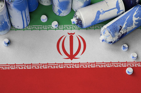Iran flag and few used aerosol spray cans for graffiti painting. Street art culture concept,...