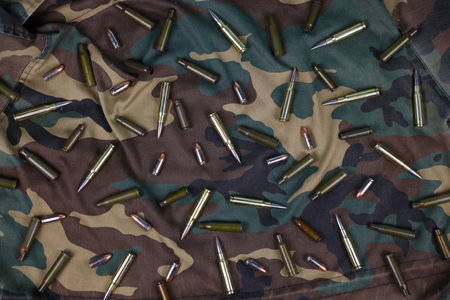 Many rifle bullets and cartridges on dark camouflage background. Concept of war action or huntingの写真素材