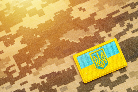 Pixeled digital military camouflage fabric with ukrainian flag and coat of arms on chevron in blue and yellow colors. Attributes of ukrainian soldier uniformの写真素材
