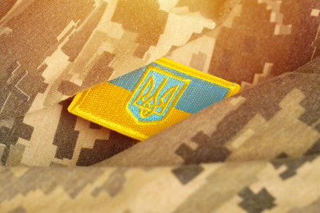 Pixeled digital military camouflage fabric with ukrainian flag and coat of arms on chevron in blue...