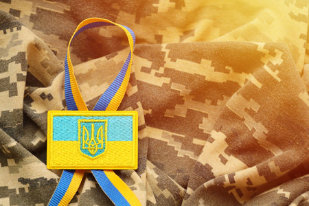 Pixeled digital military camouflage fabric with ukrainian flag and coat of arms on chevron in blue and yellow colors. Attributes of ukrainian soldier uniformの写真素材