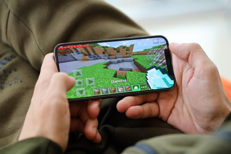 Minecraft mobile iOS game on iPhone 15 smartphone screen in male hands during mobile gameplay. Mobile gaming and entertainment on portable deviceのeditorial素材