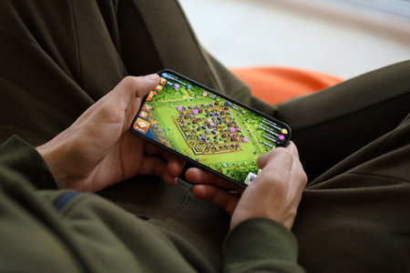 Clash of Clans mobile iOS game on iPhone 15 smartphone screen in male hands during mobile gameplay. Mobile gaming and entertainment on portable deviceのeditorial素材