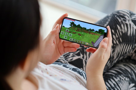 Minecraft mobile iOS game on iPhone 15 smartphone screen in female hands during mobile gameplay. Mobile gaming and entertainment on portable deviceのeditorial素材