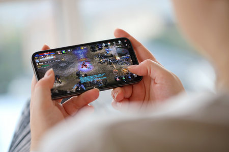 Lineage M mobile iOS game on iPhone 15 smartphone screen in female hands during mobile gameplay. Mobile gaming and entertainment on portable deviceのeditorial素材