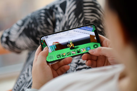 Roblox mobile iOS game on iPhone 15 smartphone screen in female hands during mobile gameplay. Mobile gaming and entertainment on portable deviceのeditorial素材