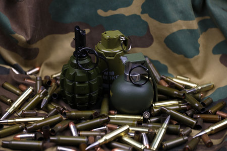 Different types of ammunition and grenades on a camouflage background. Preparing for war. Possession...