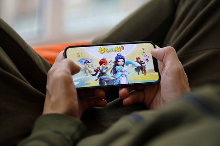 Fantasy Westward Journey mobile iOS game on iPhone 15 smartphone screen in male hands during mobile gameplay. Mobile gaming and entertainment on portable deviceのeditorial素材