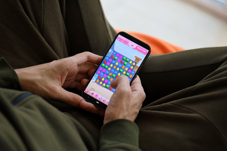 Candy Crush Saga mobile iOS game on iPhone 15 smartphone screen in male hands during mobile gameplay. Mobile gaming and entertainment on portable deviceのeditorial素材