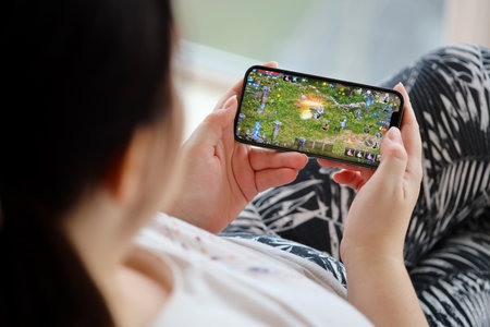 Lineage M mobile iOS game on iPhone 15 smartphone screen in female hands during mobile gameplay. Mobile gaming and entertainment on portable deviceのeditorial素材