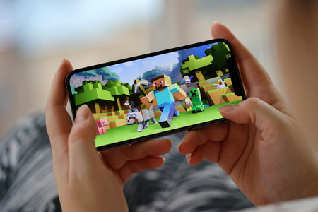 Minecraft mobile iOS game on iPhone 15 smartphone screen in female hands during mobile gameplay. Mobile gaming and entertainment on portable deviceのeditorial素材