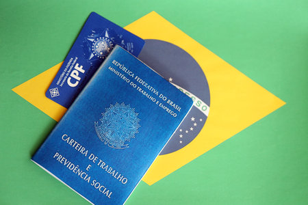 TERNOPIL, UKRAINE - JULY 7, 2023 Brazilian Work Permit document and Brazilian tax number card on table with flagのeditorial素材