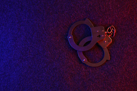 Closed handcuffs on the dark surface at night with police car lights high contrast imageの写真素材