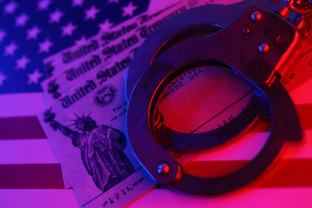US Tax refund check and handcuffs on flag of United States of America close up. Record criminal...