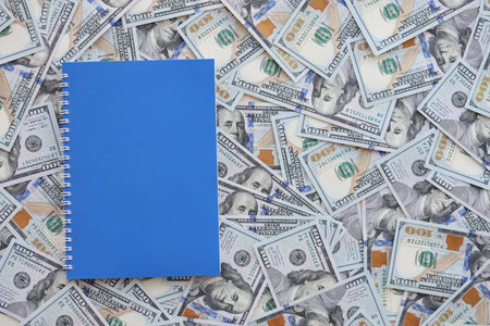 Office workplace table with blank notebook or notepad and many hundred dollar bills close up