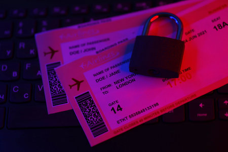 Fictional air tickets and small padlock on computer keyboard close up