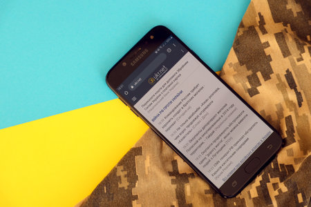 KYIV, UKRAINE - 4 MAY, 2023: Ukr Net ukrainian news portal on smartphone screen with ukrainian flag and camouflage fabric close upのeditorial素材