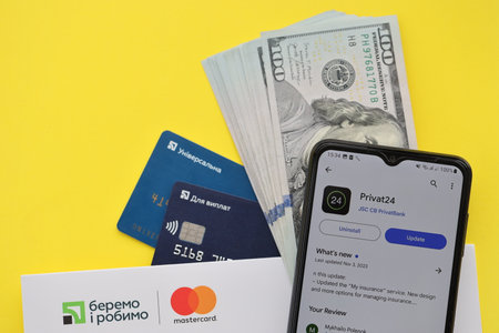 TERNOPIL, UKRAINE - JULY 7, 2023 Privatbank new banking plastic cards with money on table. Privat24 application close upのeditorial素材