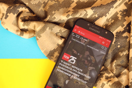 KYIV, UKRAINE - 4 MAY, 2023: TSN ukrainian news portal on smartphone screen with ukrainian flag and camouflage fabric close upのeditorial素材