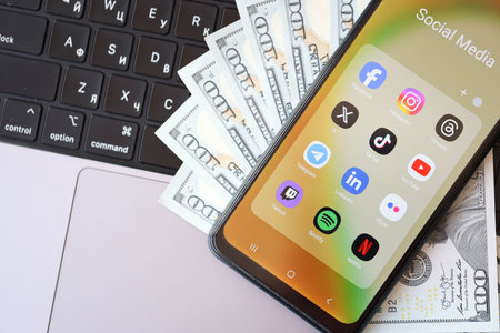 KYIV, UKRAINE - FEBRUARY 28, 2024 Social Media icons group on Galaxy A04s smartphone display on MacBook keyboard and US Dollar billsのeditorial素材