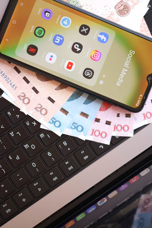 KYIV, UKRAINE - FEBRUARY 28, 2024 Social Media icons group on Galaxy A04s smartphone display on MacBook keyboard and Chinese Yuan money billsのeditorial素材