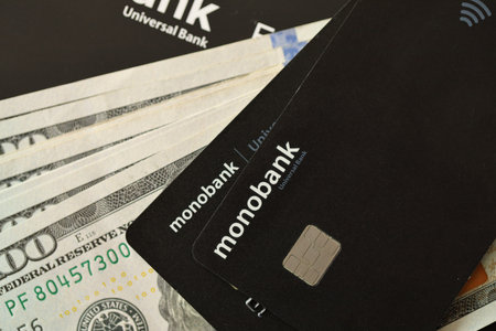KYIV, UKRAINE - JULY 7, 2023 Monobank black banking plastic cards with money on tableのeditorial素材