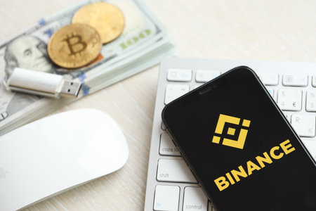 KYIV, UKRAINE - MARCH 15, 2024 Binance logo on iPhone display screen on white keyboard with money and bitcoins. Cryptocurrency exchange portalのeditorial素材