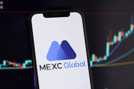 KYIV, UKRAINE - MARCH 15, 2024 MEXC logo on iPhone display screen and crypto currency value charts. Cryptocurrency exchange portalのeditorial素材