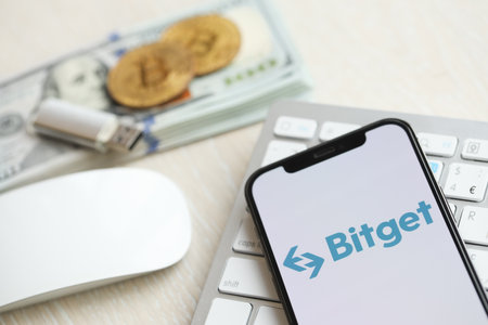 KYIV, UKRAINE - MARCH 15, 2024 Bitget logo on iPhone display screen on white keyboard with money and bitcoins. Cryptocurrency exchange portalのeditorial素材