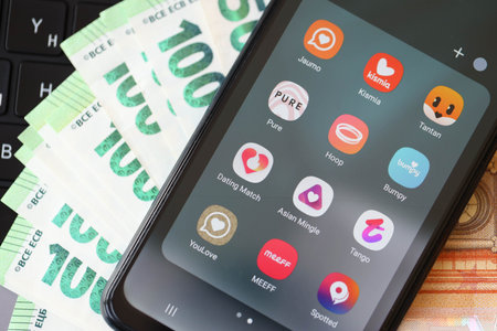 KYIV, UKRAINE - FEBRUARY 28, 2024 Dating apps icons on smartphone display on MacBook keyboard and euro billsのeditorial素材