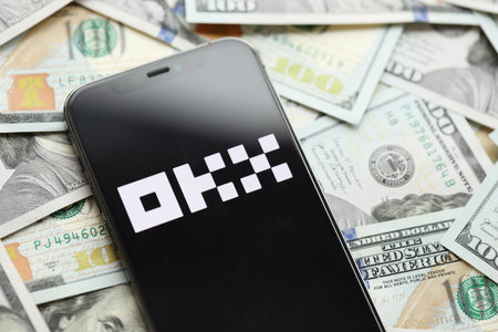 KYIV, UKRAINE - MARCH 15, 2024 OKX logo on iPhone display screen with many hundred dollar bills. Cryptocurrency exchange portalのeditorial素材