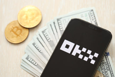 KYIV, UKRAINE - MARCH 15, 2024 OKX logo on iPhone display screen with dollars and bitcoins on table. Cryptocurrency exchange portalのeditorial素材